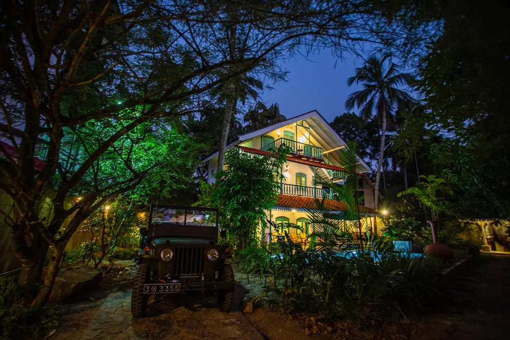 Vintage jeep parked in the garden with the lit villa behind it