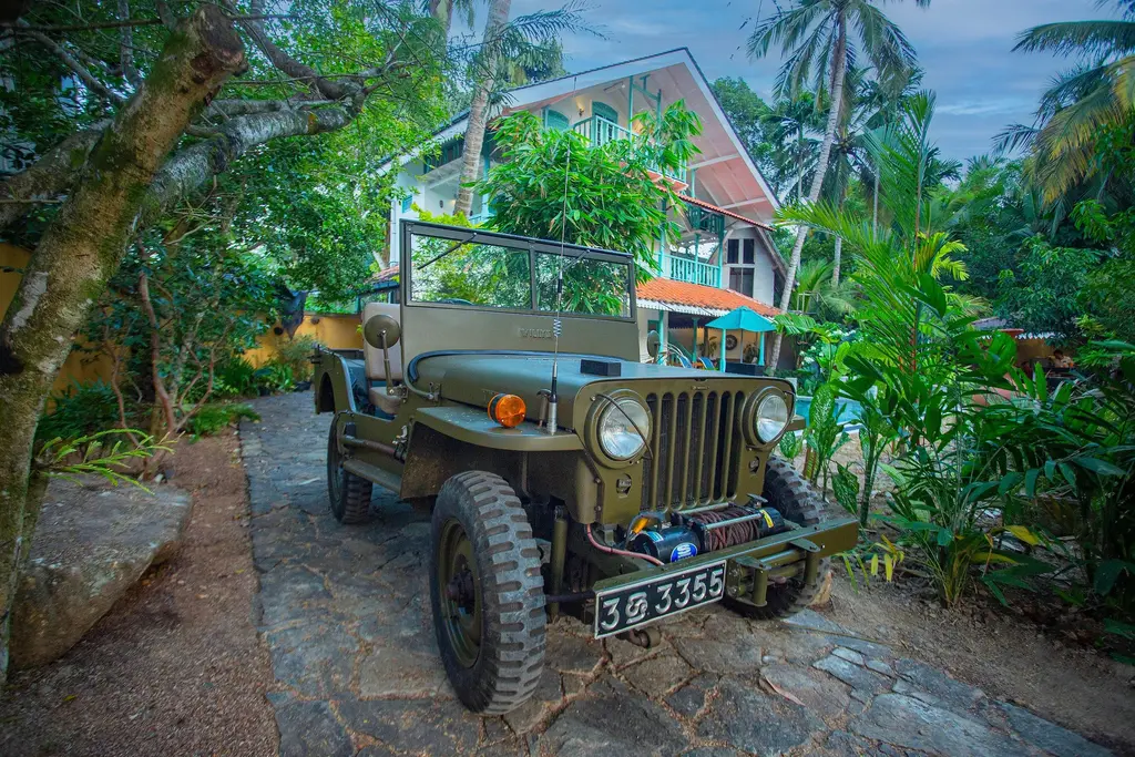 Vintage army-green jeep on the stone driveway among tropical plants