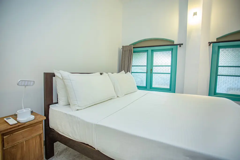 Bright double bedroom with white linen and turquoise windows