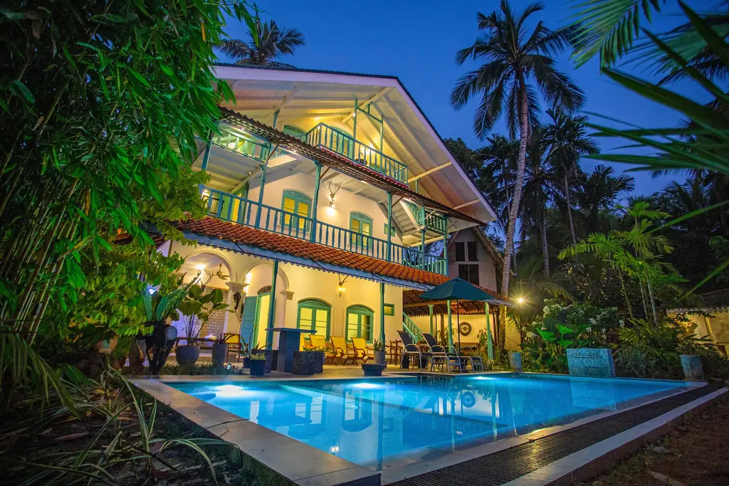 The villa and pool lit up at night under coconut palms